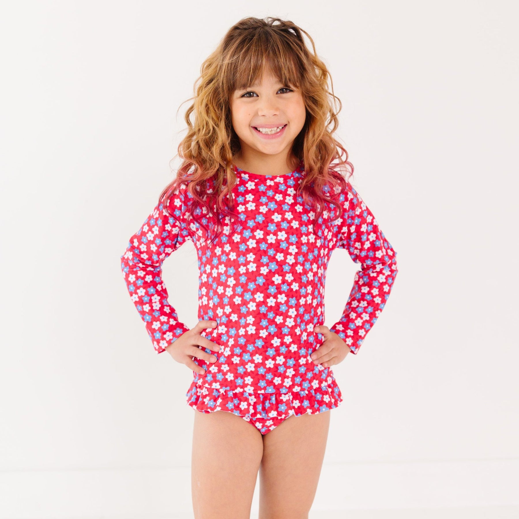 Young girl wearing a red floral swimsuit with long sleeves on a white background