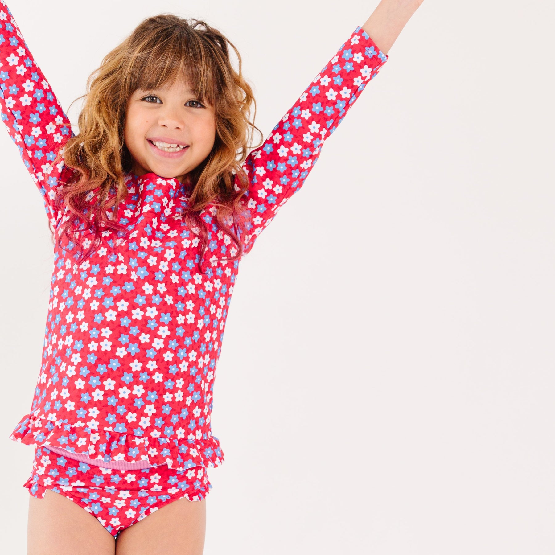 Young girl wearing a red and white floral swimsuit on a white background