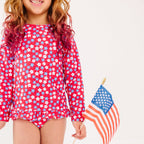 Young girl wearing a red, white, and blue floral swimsuit holding an American flag.
