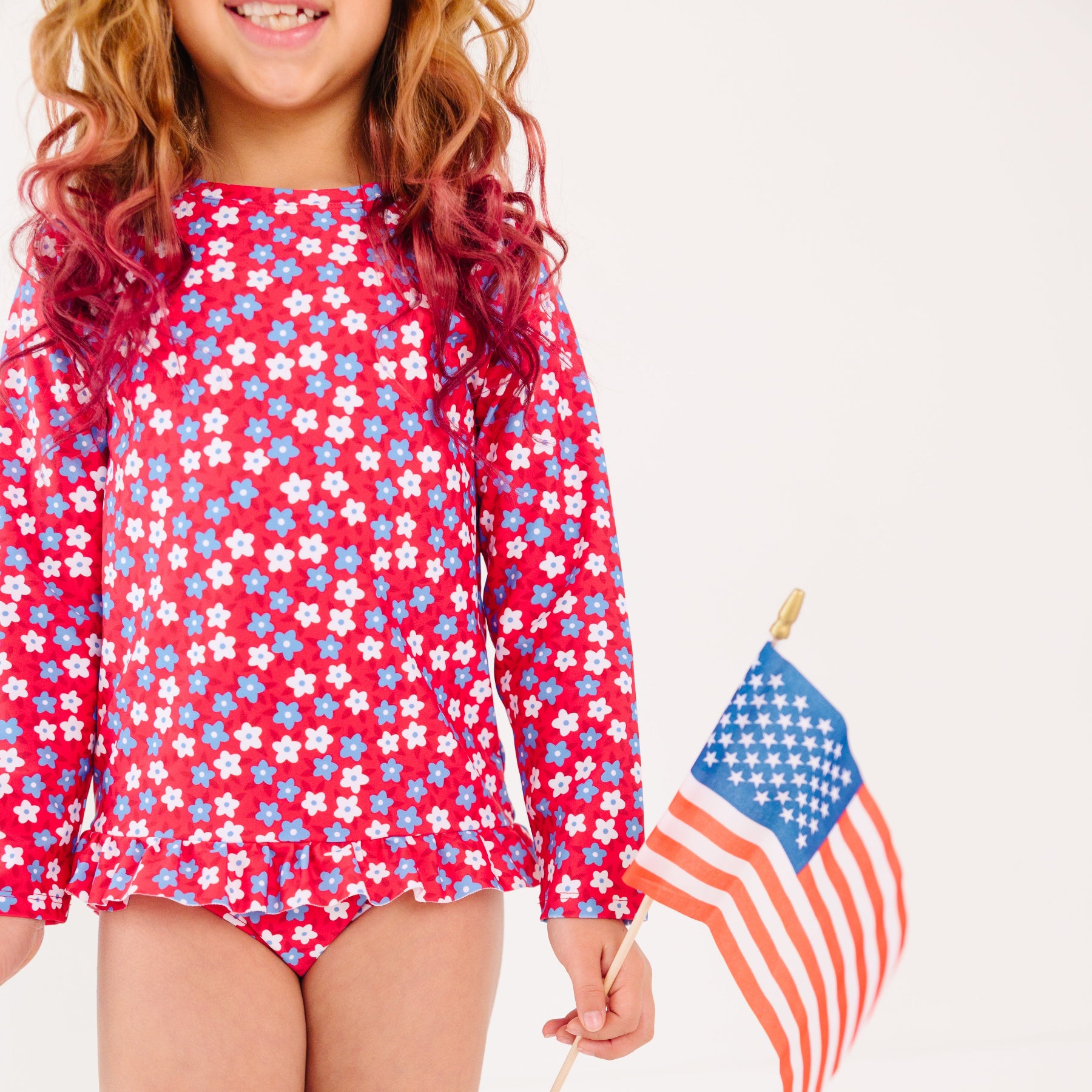 Young girl wearing a red, white, and blue floral swimsuit holding an American flag.