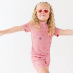 Child wearing a pink shorts pajama set with heart sunglasses on a white background