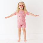 Child wearing a pink shorts pajama set with heart sunglasses on a white background
