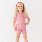 Child wearing a pink shorts pajama set with heart sunglasses on a white background