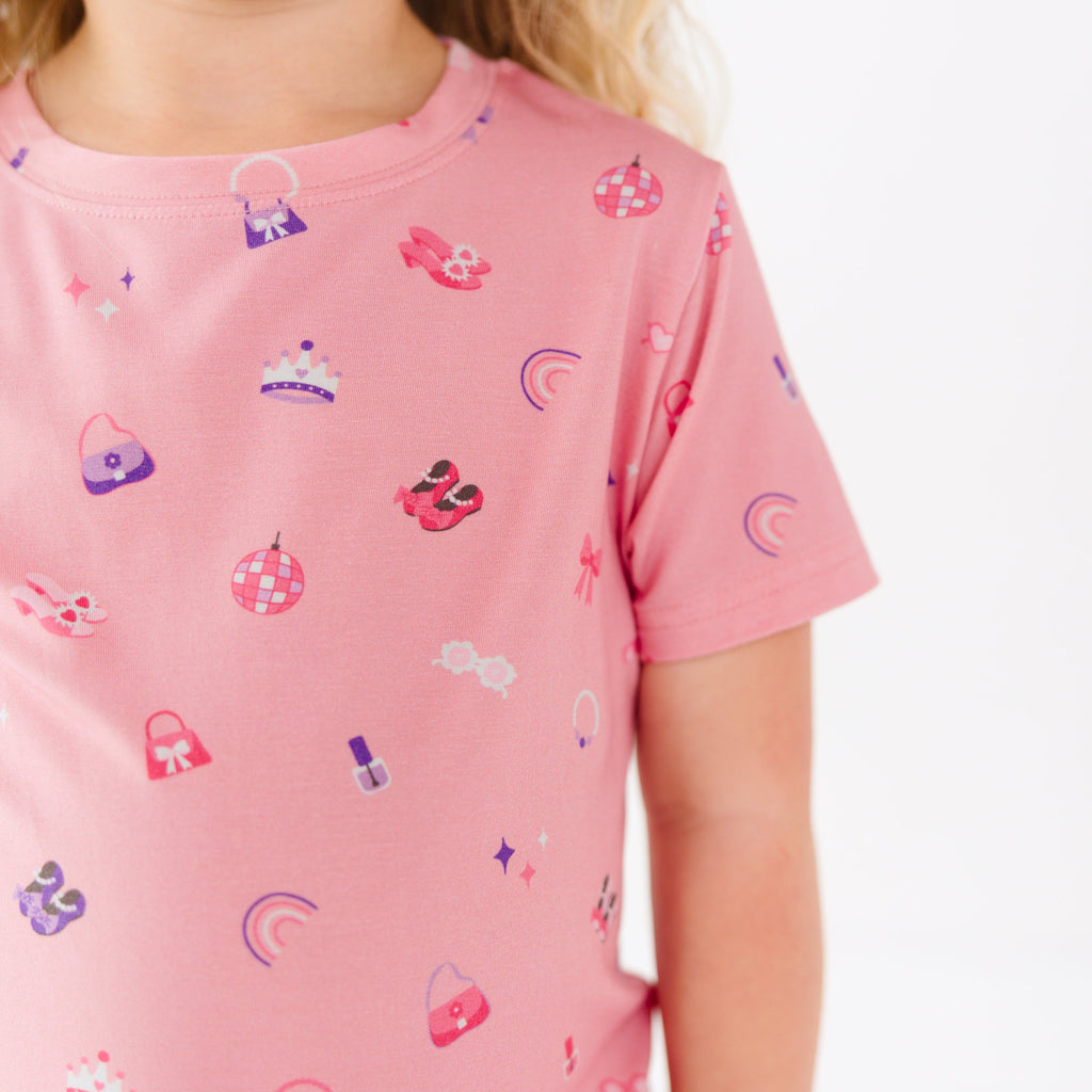Close up of a pink shirt with various small icons worn by a young girl on a white background