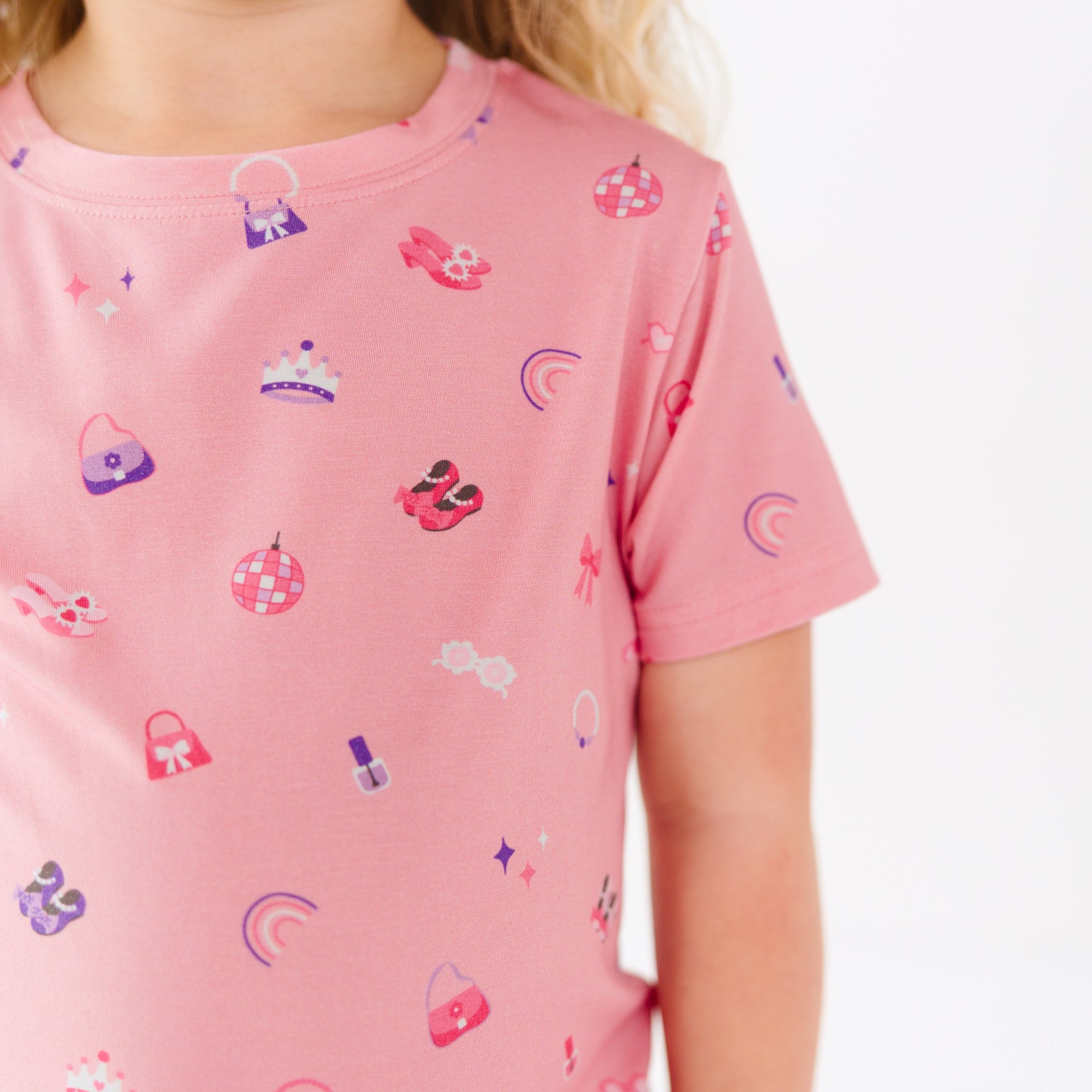 Close up of a pink shirt with various small icons worn by a young girl on a white background