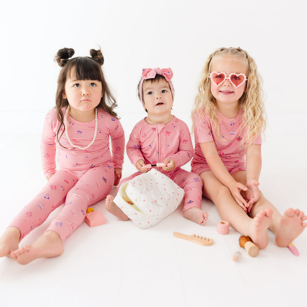 Three children in pink outfits sitting on a white surface with a white background