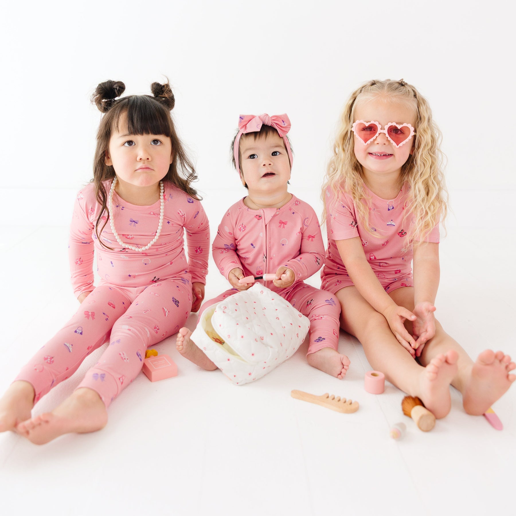 Three children in pink outfits sitting on a white surface with a white background