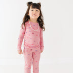 Young girl wearing pink pajamas with girly patterns on a white background