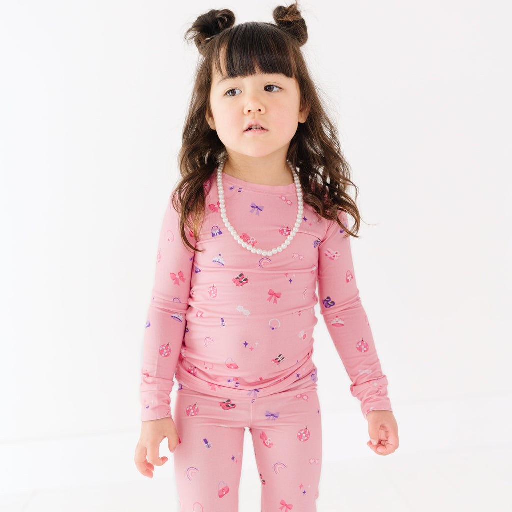 Child wearing a pink pajama set with girly  patterns on a white background