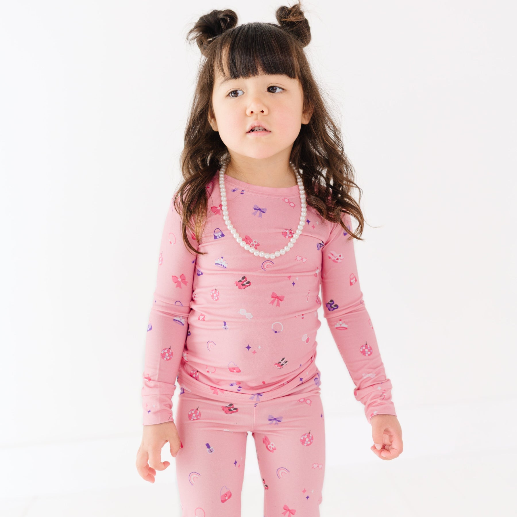 Child wearing a pink pajama set with girly  patterns on a white background