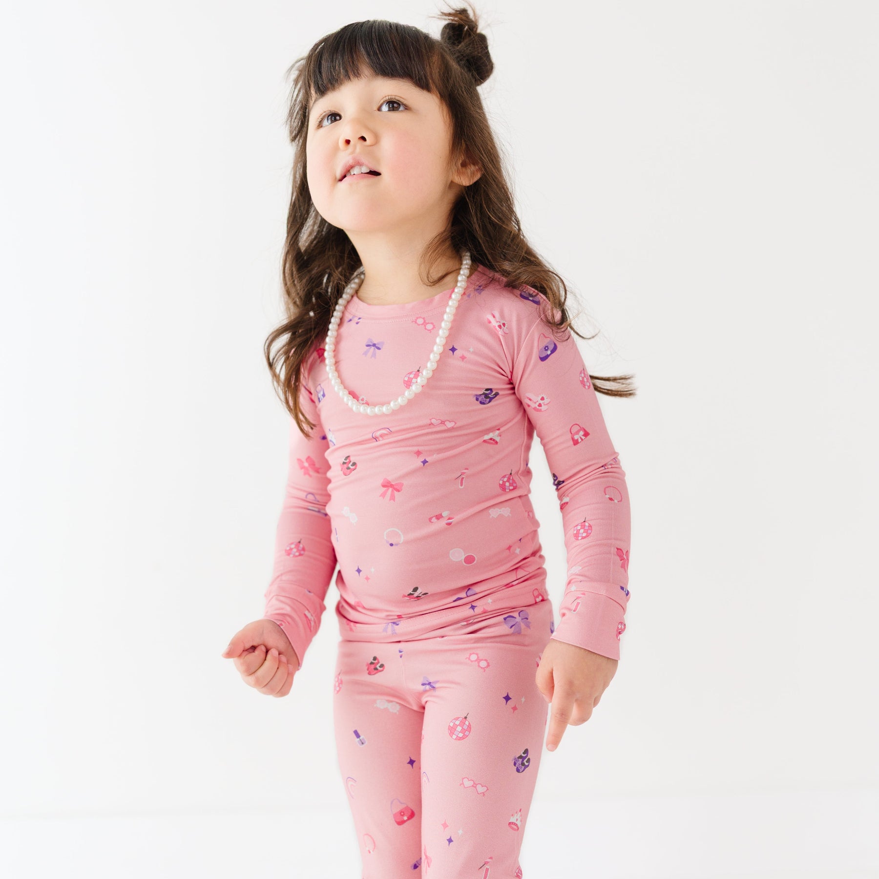 Child wearing a pink pajama set with girly patterns on a white background