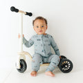Child sitting on a scooter wearing a onesie with bicycles and scooters print