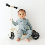 Child sitting on a scooter wearing a onesie with bicycles and scooters print