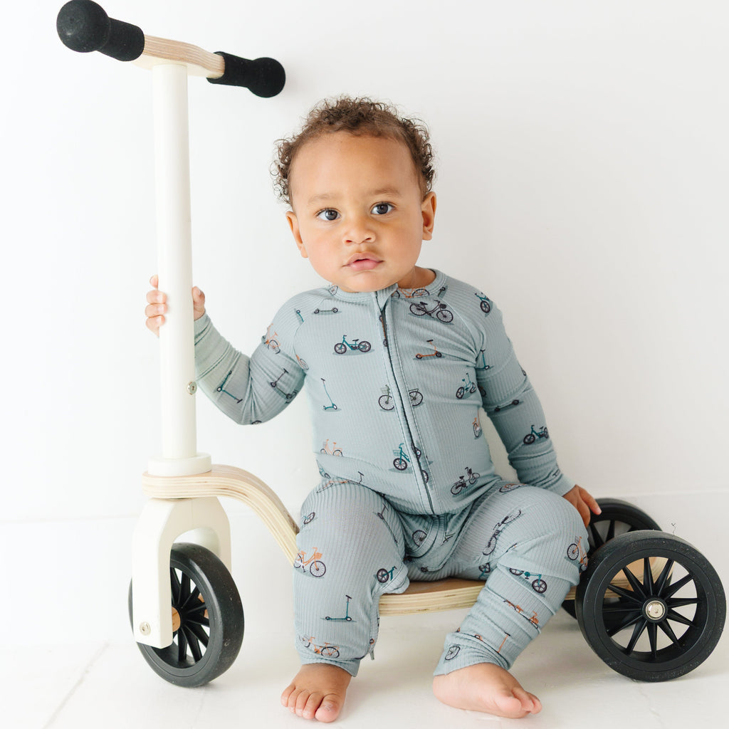 Child sitting on a scooter wearing a onesie with bicycles and scooters print
