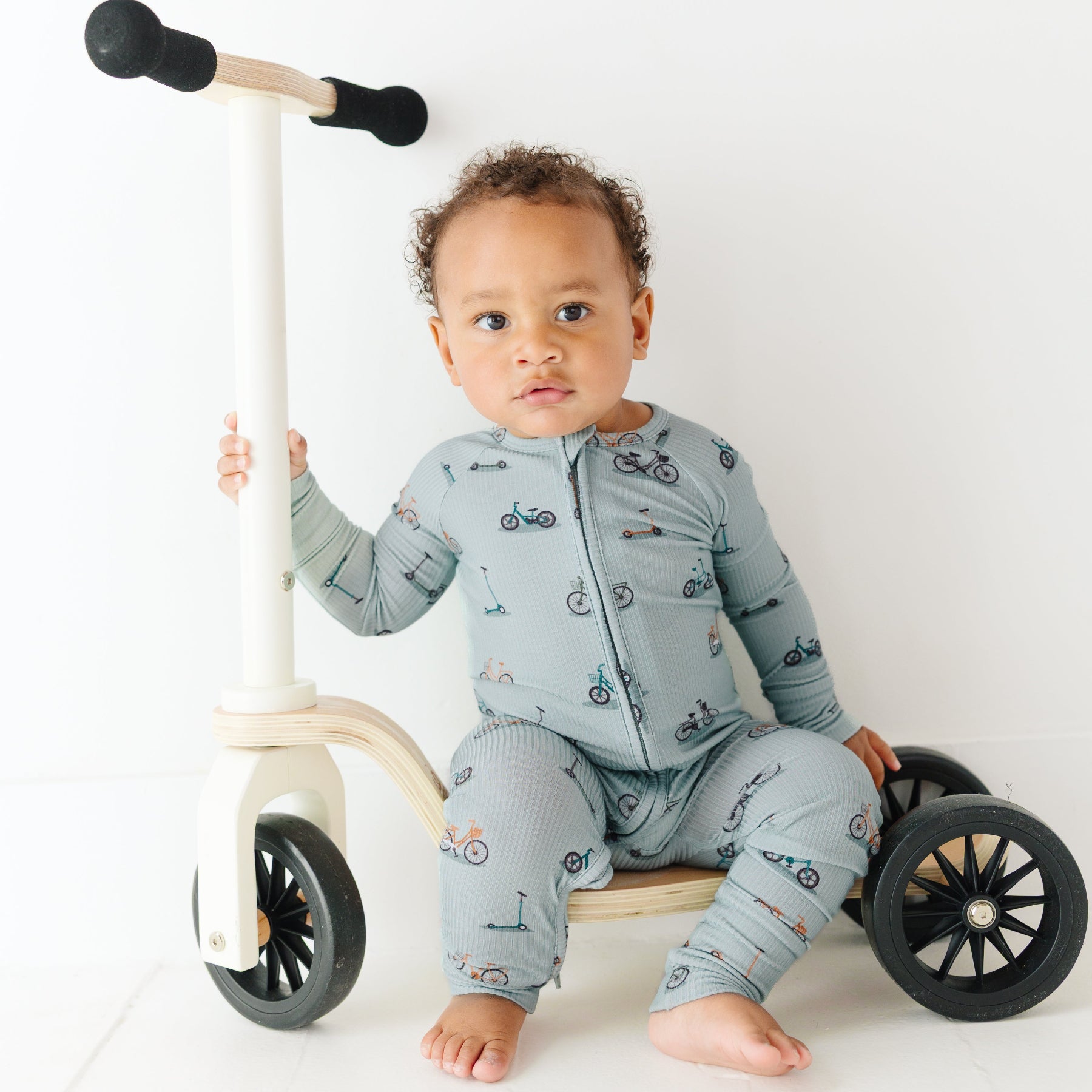 Child sitting on a scooter wearing a onesie with bicycles and scooters print