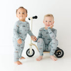 Two children wearing matching pajamas standing next to a small bike on a white background