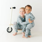 Two children wearing matching pajamas standing next to a small bike on a white background