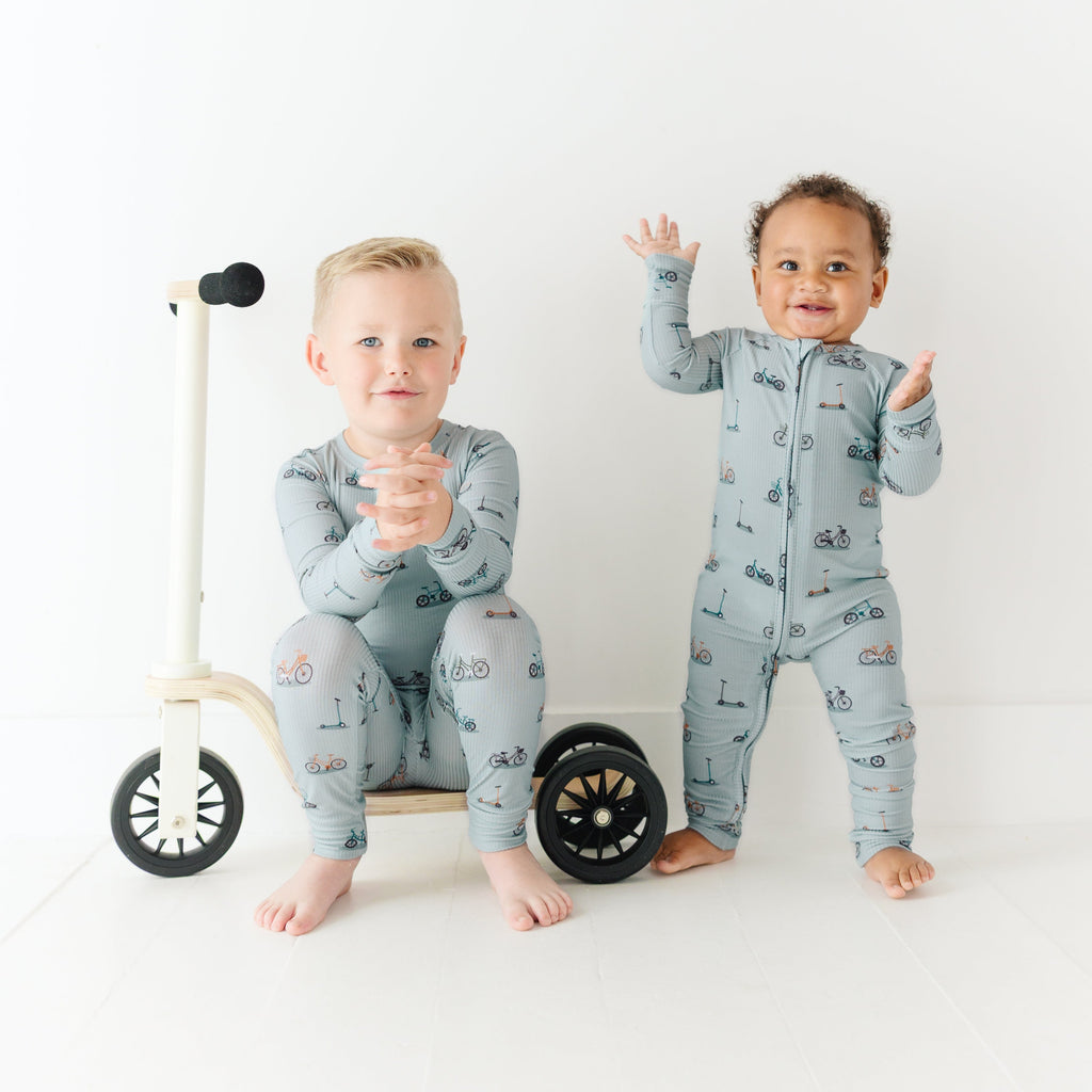 Two children wearing matching pajamas standing next to a small bike on a white background