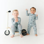 Two children wearing matching pajamas standing next to a small bike on a white background