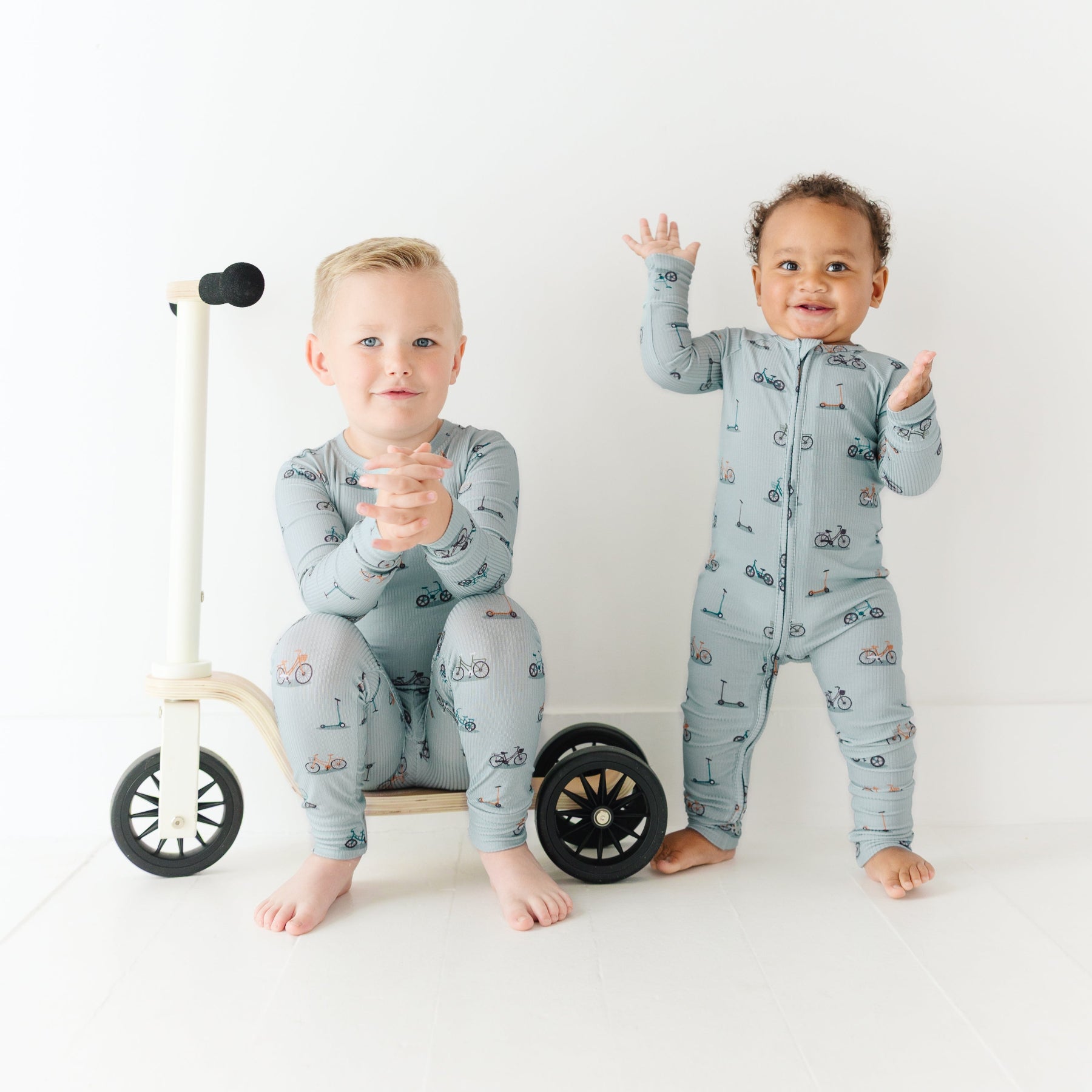 Two children wearing matching pajamas standing next to a small bike on a white background