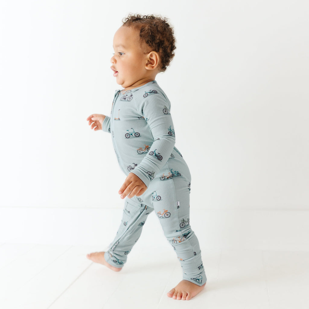 Child wearing a light blue onesie with vehicle patterns on a white background