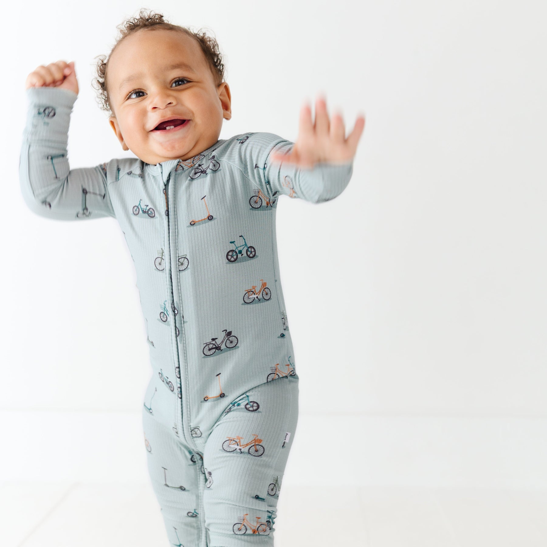 Child wearing a light blue onesie with vehicle patterns on a white background