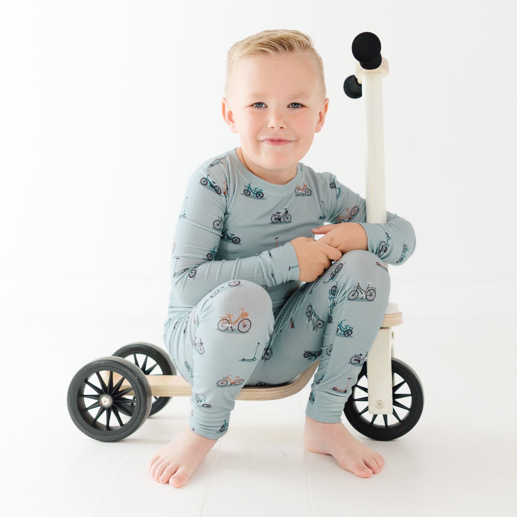 Child sitting on a wooden balance bike with wheels on a white background