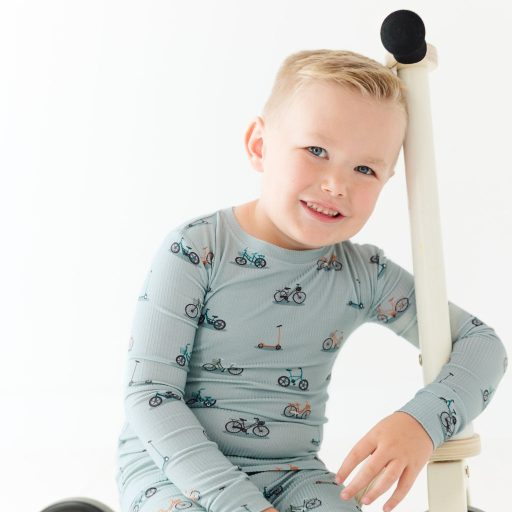 Child wearing a light blue long-sleeve shirt with bicycle pattern, sitting on a scooter.