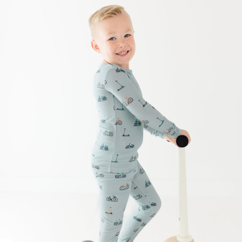 Child in patterned pajamas standing with a balance bike on a white background