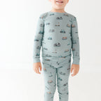 Child wearing a light blue pajama set with vehicle pattern on a white background