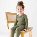 Child wearing olive Two-Piece set sitting on a wooden chair with a white background