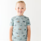 Child wearing a light blue outfit with bicycles & scooter patterns on a plain background