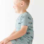 Child wearing a light blue outfit with bicycles & scooter patterns on a plain background