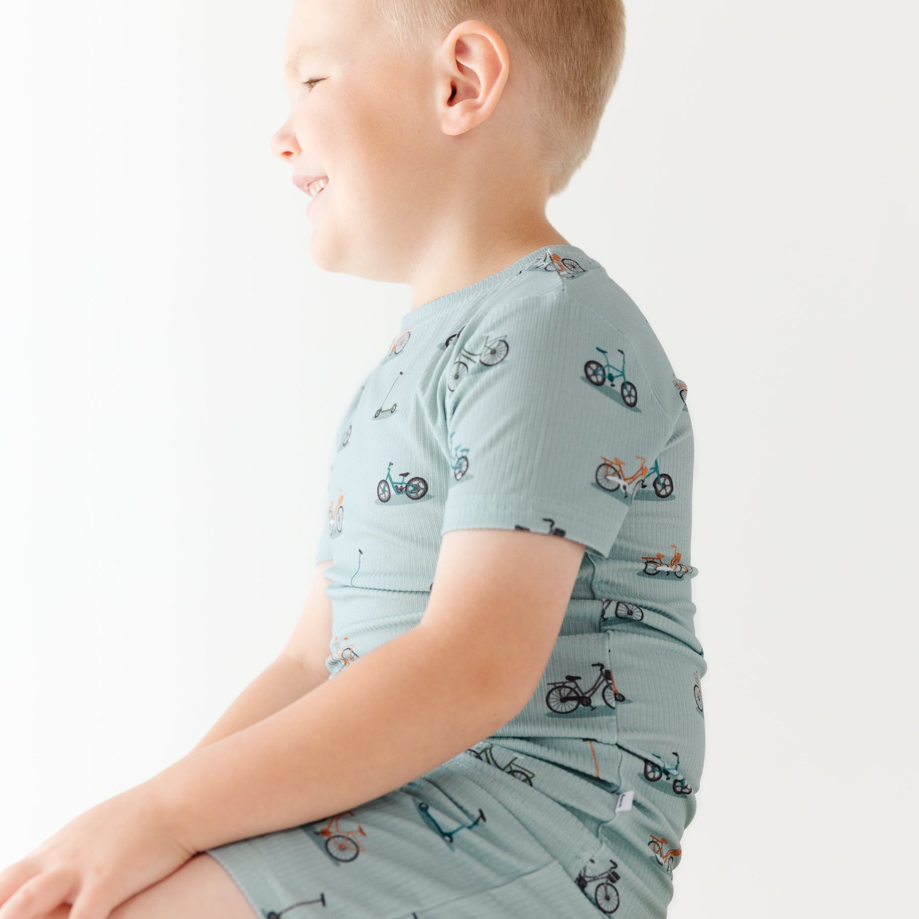Child wearing a light blue outfit with bicycles & scooter patterns on a plain background