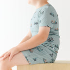 Child wearing a light blue outfit with bicycle pattern sitting on a wooden surface