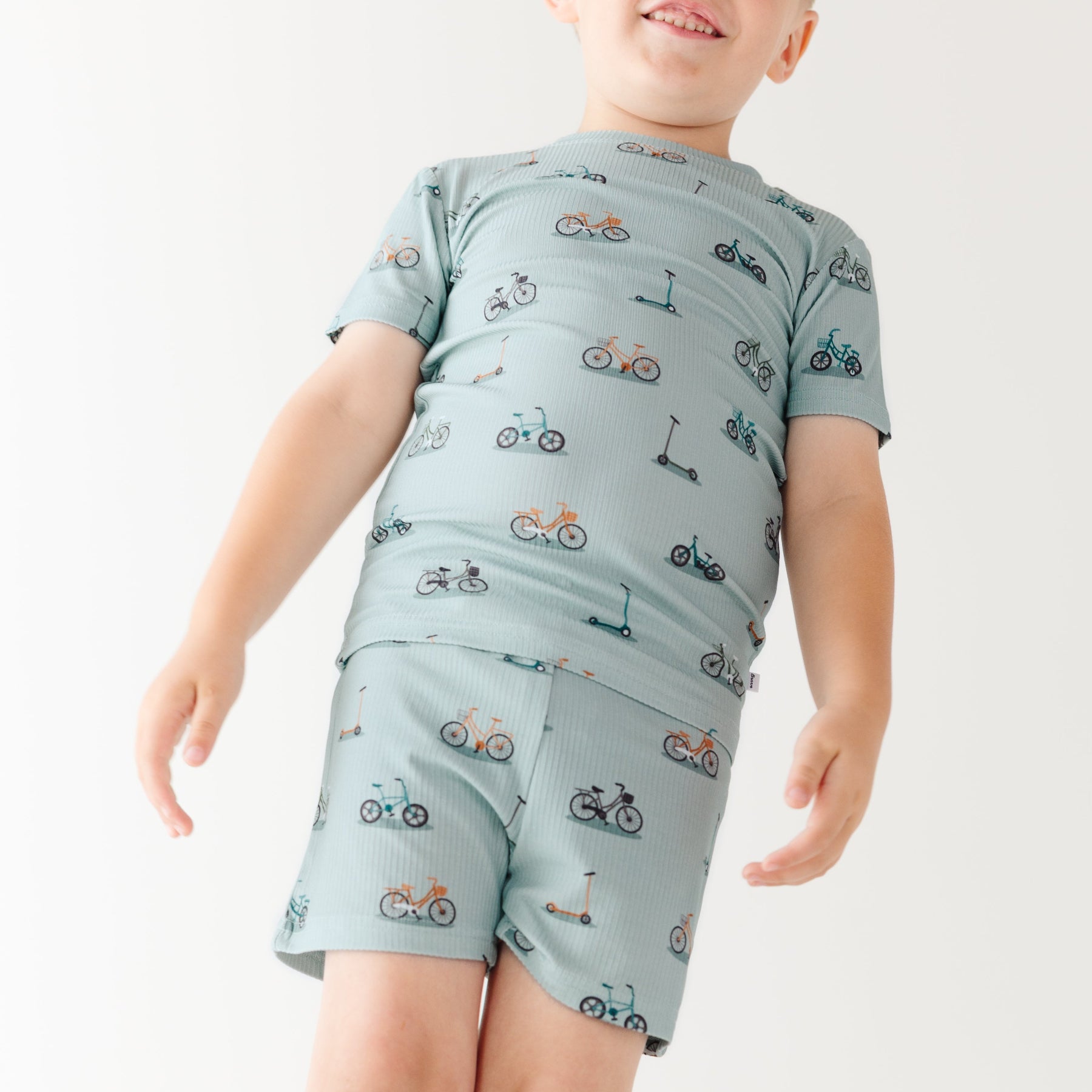 Child wearing a light blue outfit with bicycles & scooter patterns on a plain background