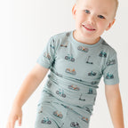 Child wearing a light blue outfit with bicycles & scooter patterns on a plain background