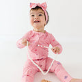 Baby in pink onesie with girly patterns holding a string of beads on a white background