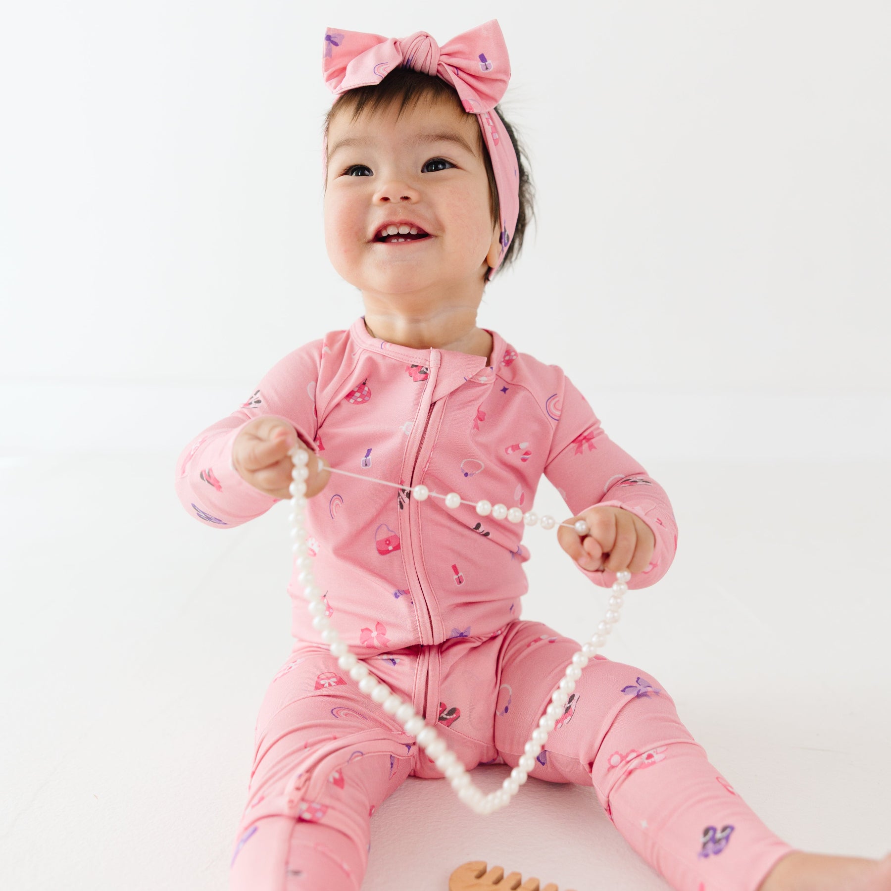 Baby in pink onesie with girly patterns holding a string of beads on a white background