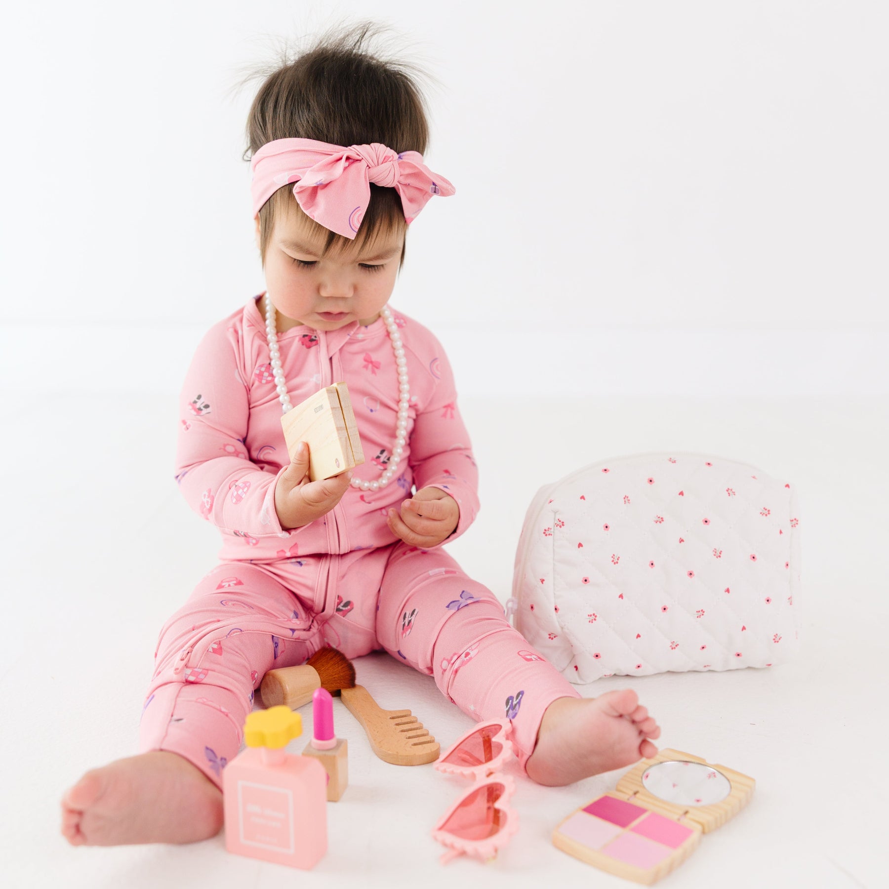 Child in pink onesie playing with girly toys on a white background
