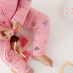Close up of a child wearing pink onesie with girly patterns, sitting on a white surface.