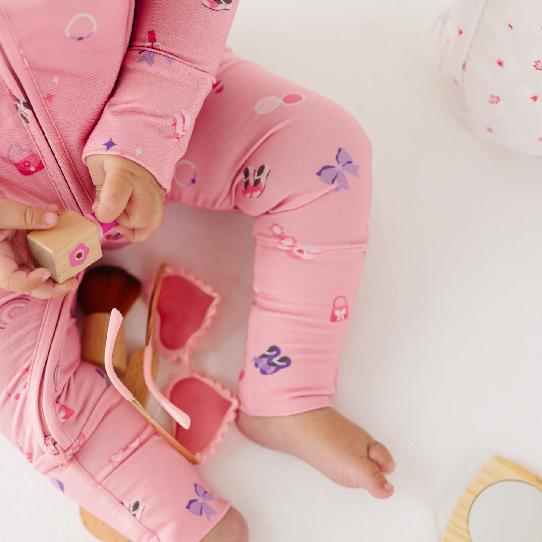 Close up of a child wearing pink onesie with girly patterns, sitting on a white surface.