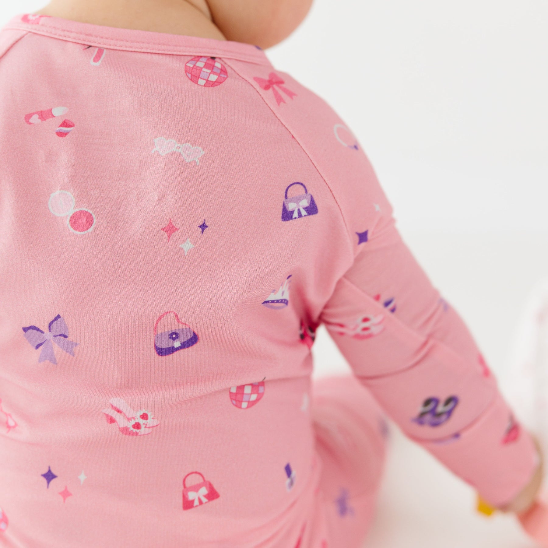 Close up of a child wearing a pink long-sleeve onesie with colorful patterns on a white background