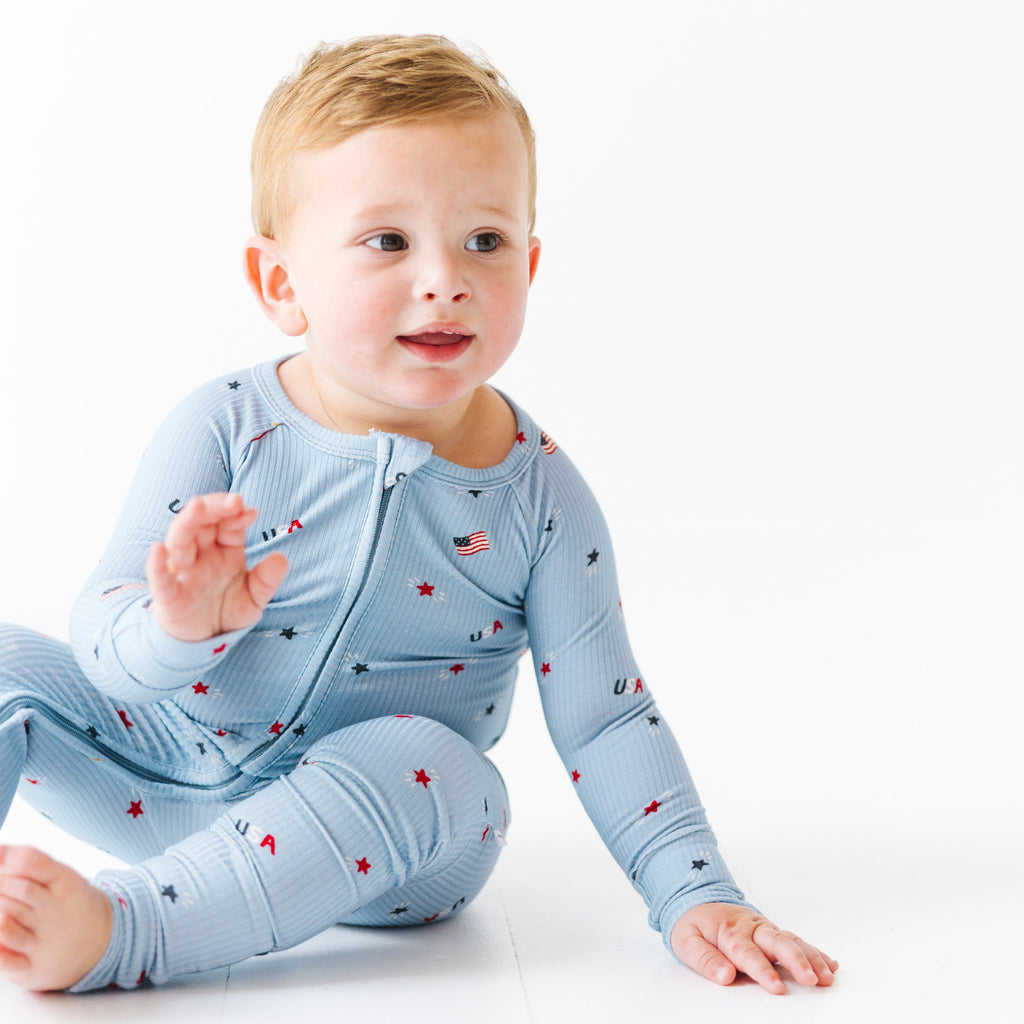 Child wearing a light blue onesie with stars and flag patterns on a white background