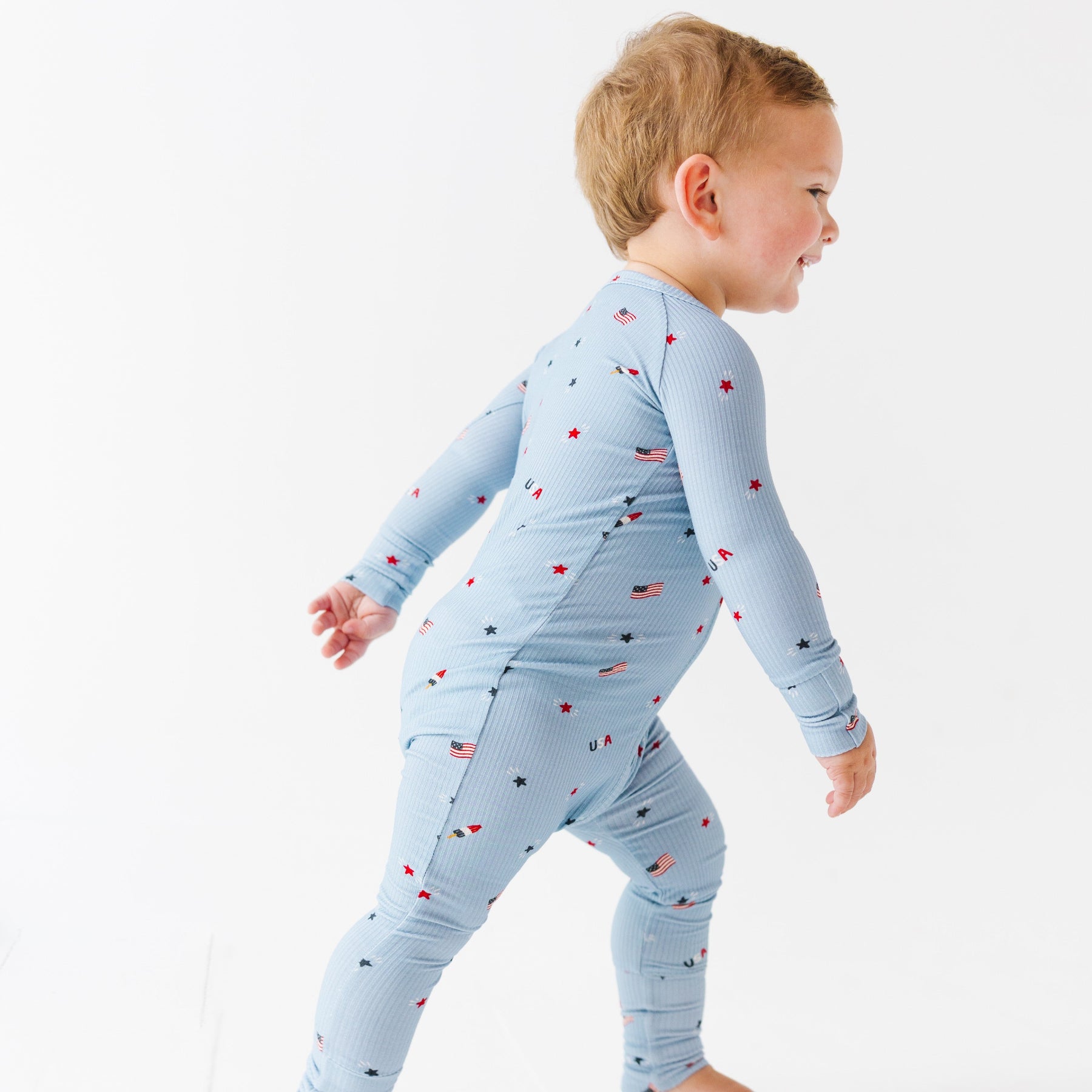 Child wearing a light blue onesie with stars and flag patterns on a white background