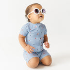 Child in blue short romper with star pattern, wearing sunglasses on a white background