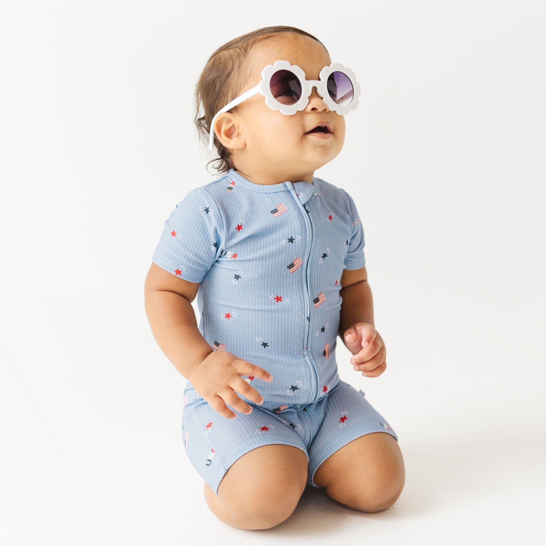 Child in blue short romper with star pattern, wearing sunglasses on a white background