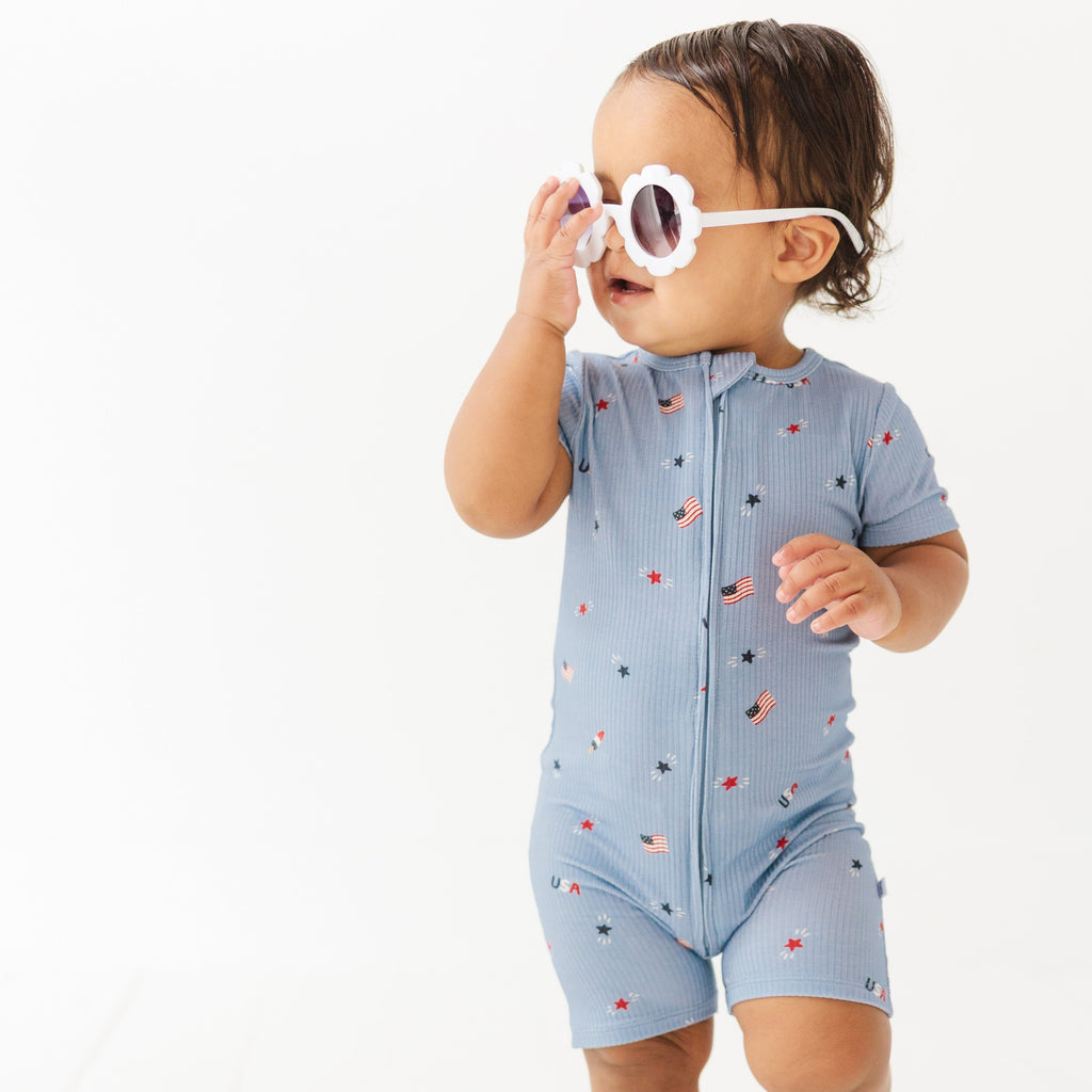 Child in blue short romper with star pattern, wearing sunglasses on a white background