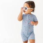 Child in blue short romper with star pattern, wearing sunglasses on a white background