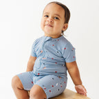 Child wearing a short romper with American-themed pattern sitting on a wooden stool.